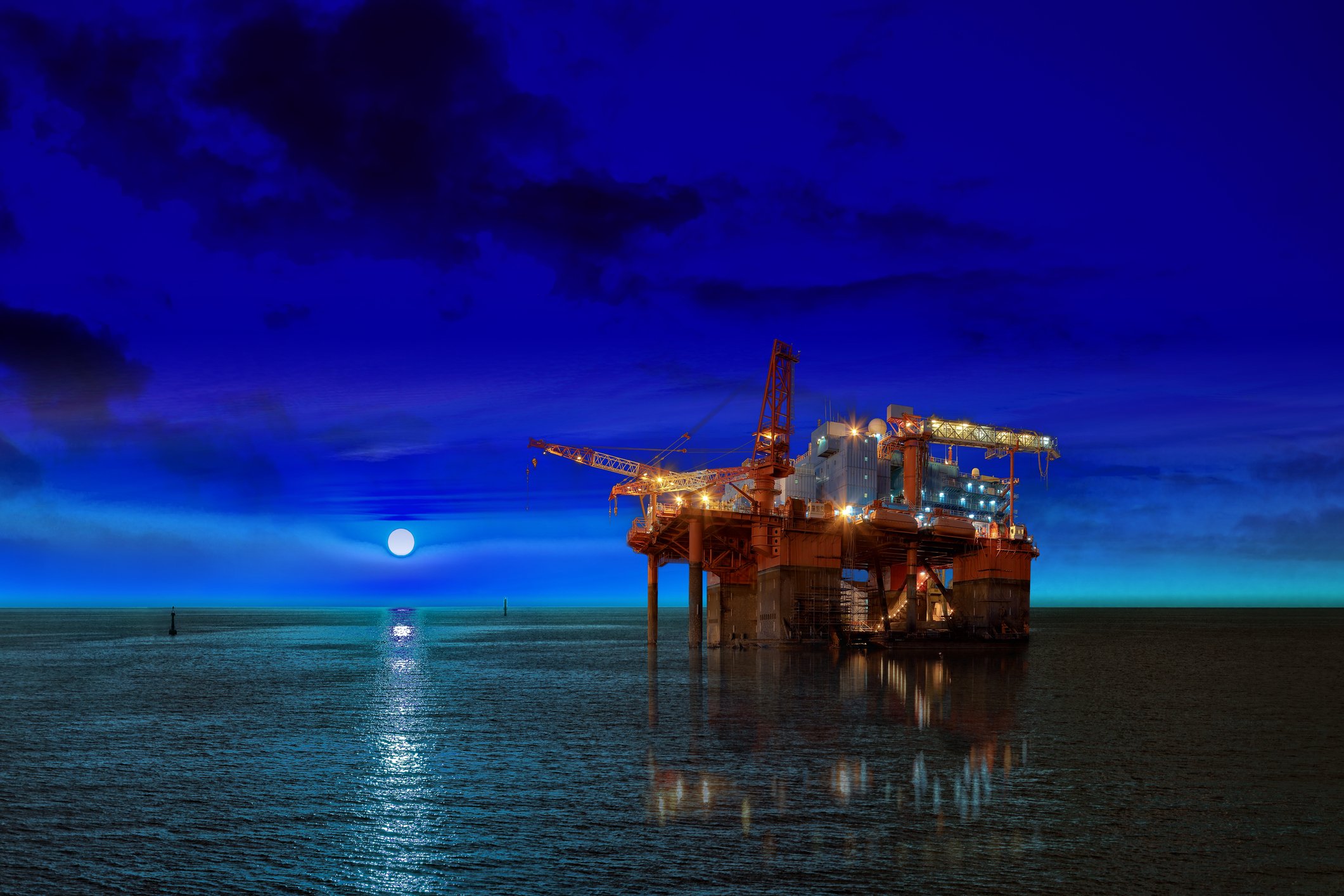 An oil rig at night time with the moon.