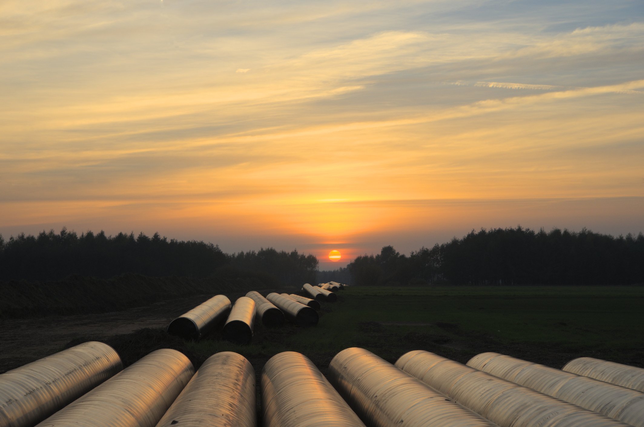 Pipeline segments laid out for construction, against the backdrop of a setting sun.