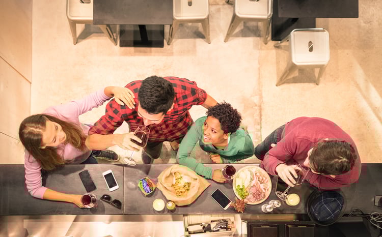 Overhead shot of friends eating and drinking wine with mobile devices on bar.