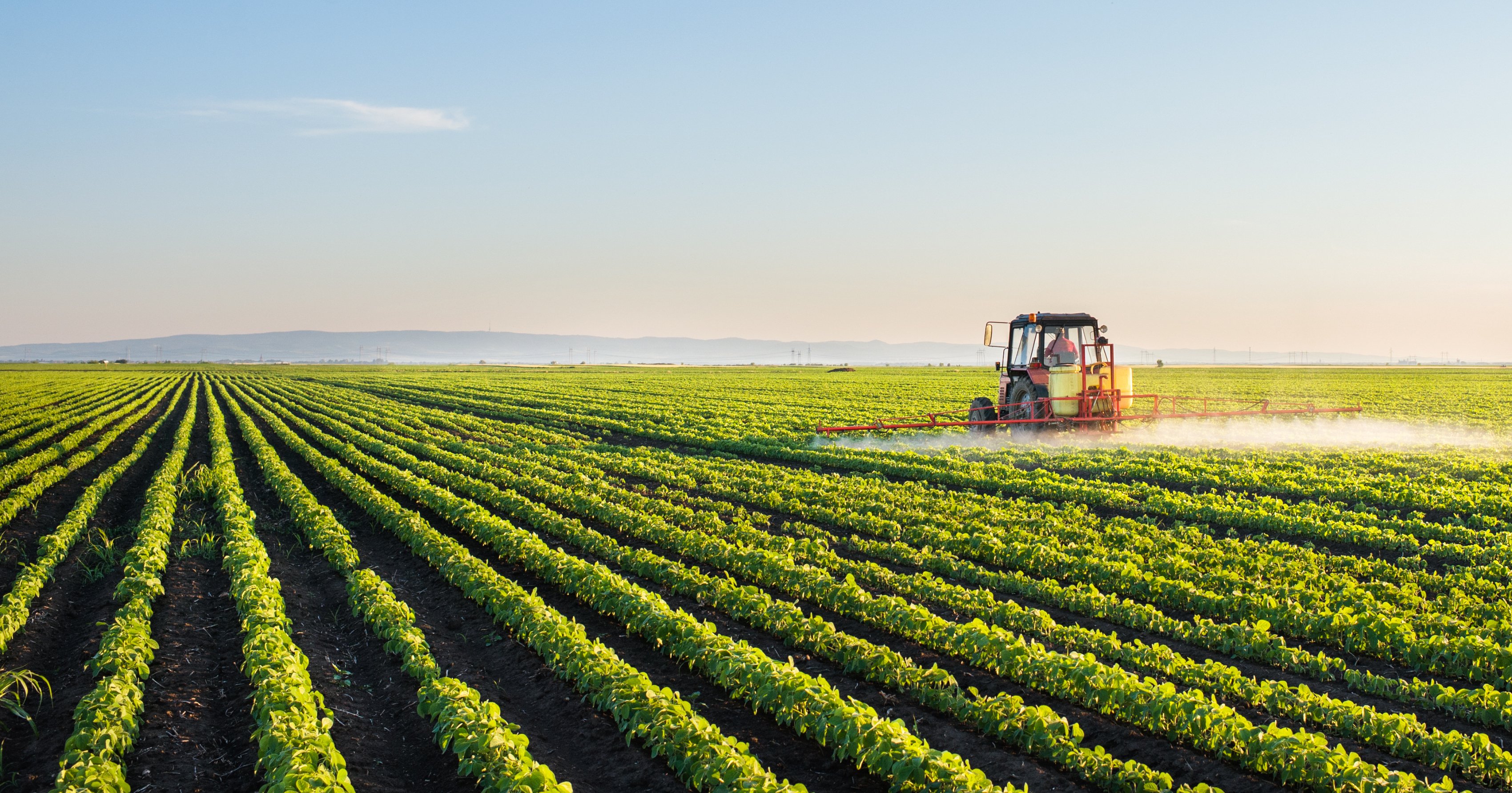 A green farming field with a tractor driving over it. 