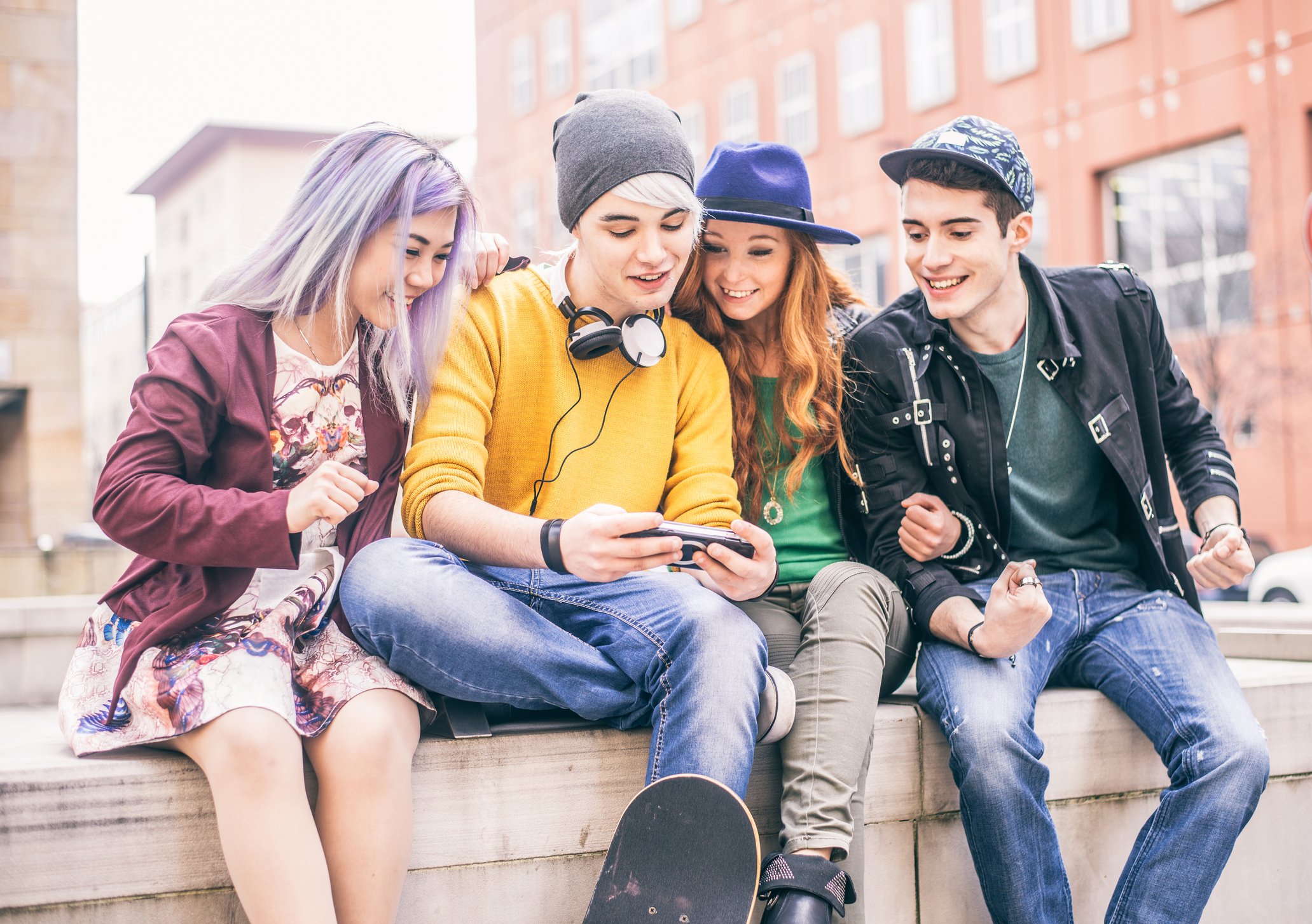Young people gathered around a friend using a cellphone.