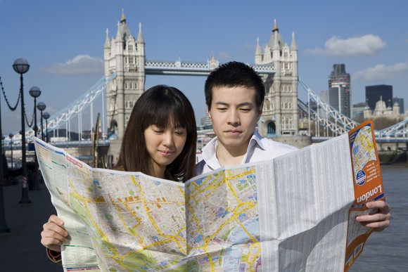 Two tourists at Tower Bridge look at an unfolded paper map.