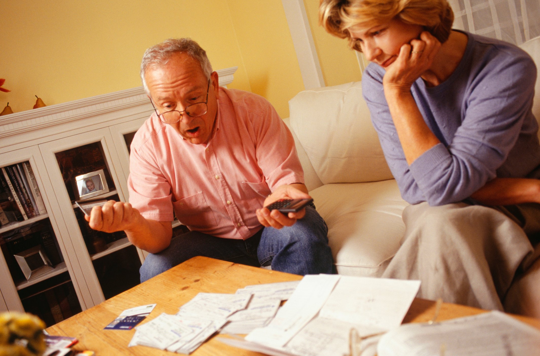 Couple sitting by table covered in papers, looking worried.