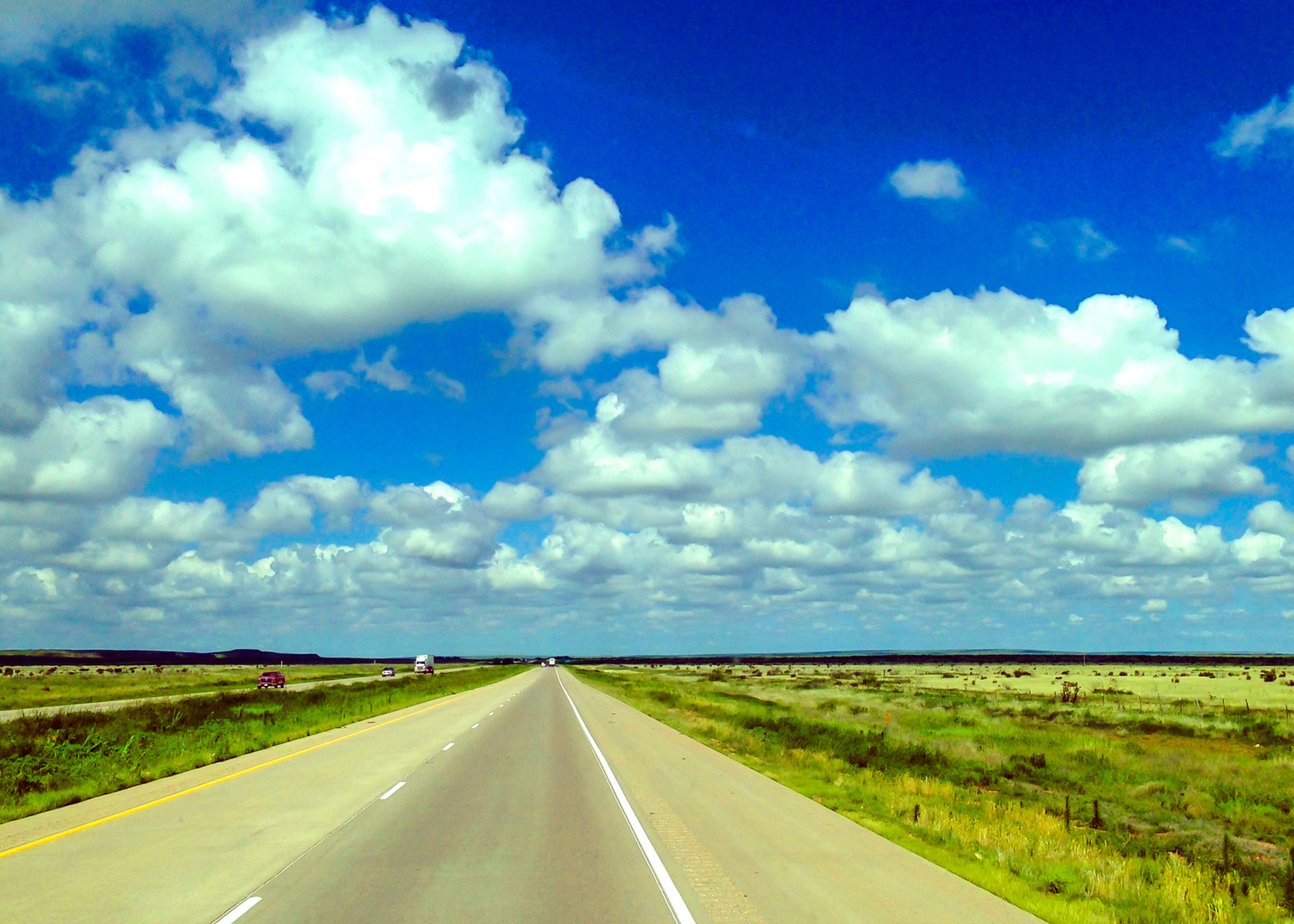 Open-road highway in North Dakota under a blue sky with white puffy clouds