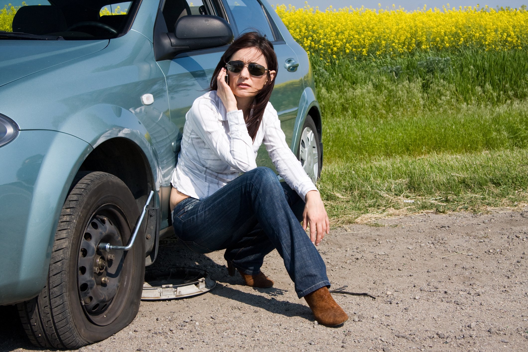 Woman calling on a cell phone next to a flat tire