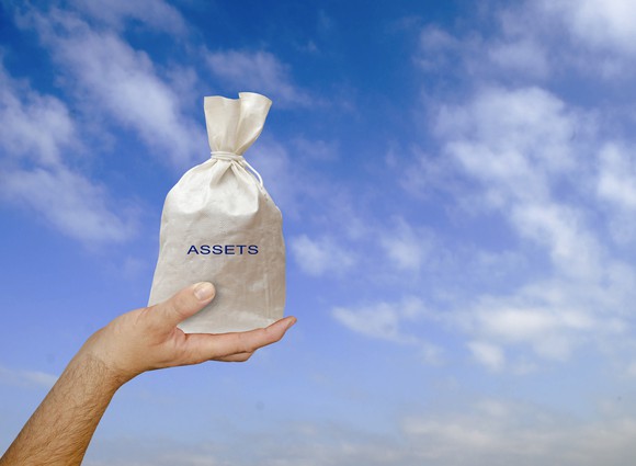 A hand holds up a bag labeled "assets" against a cloudy sky.