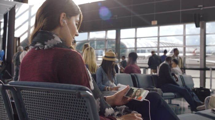 Woman in an airport watching Netflix on a smartphone.