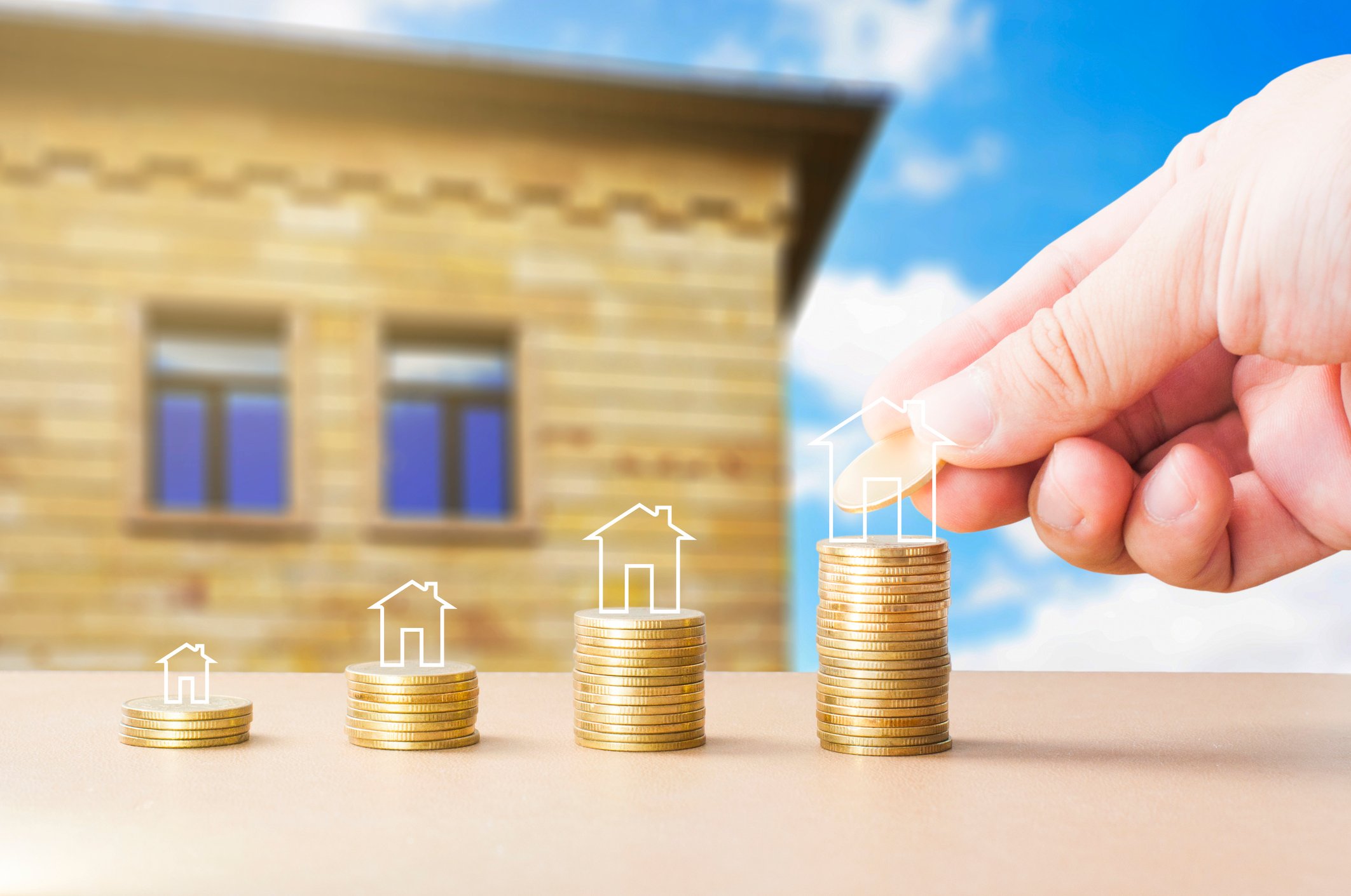 Hand stacking coins in front of house.