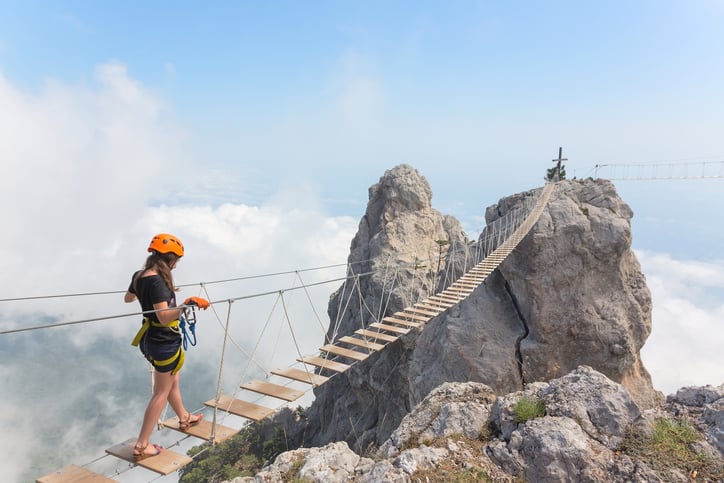 Young woman crossing walking bridge over mountain abyss in British Columbia.