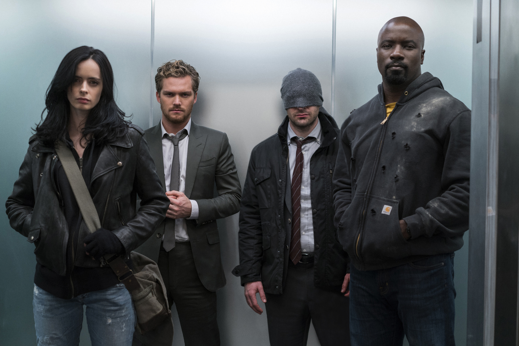 Jessica Jones, Danny Rand, Matt Murdock, and Luke Cage standing in a stainless steel elevator.