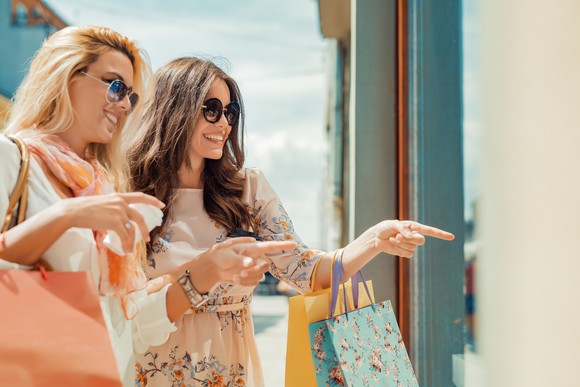 Two women holding shopping bags and pointing at a store window
