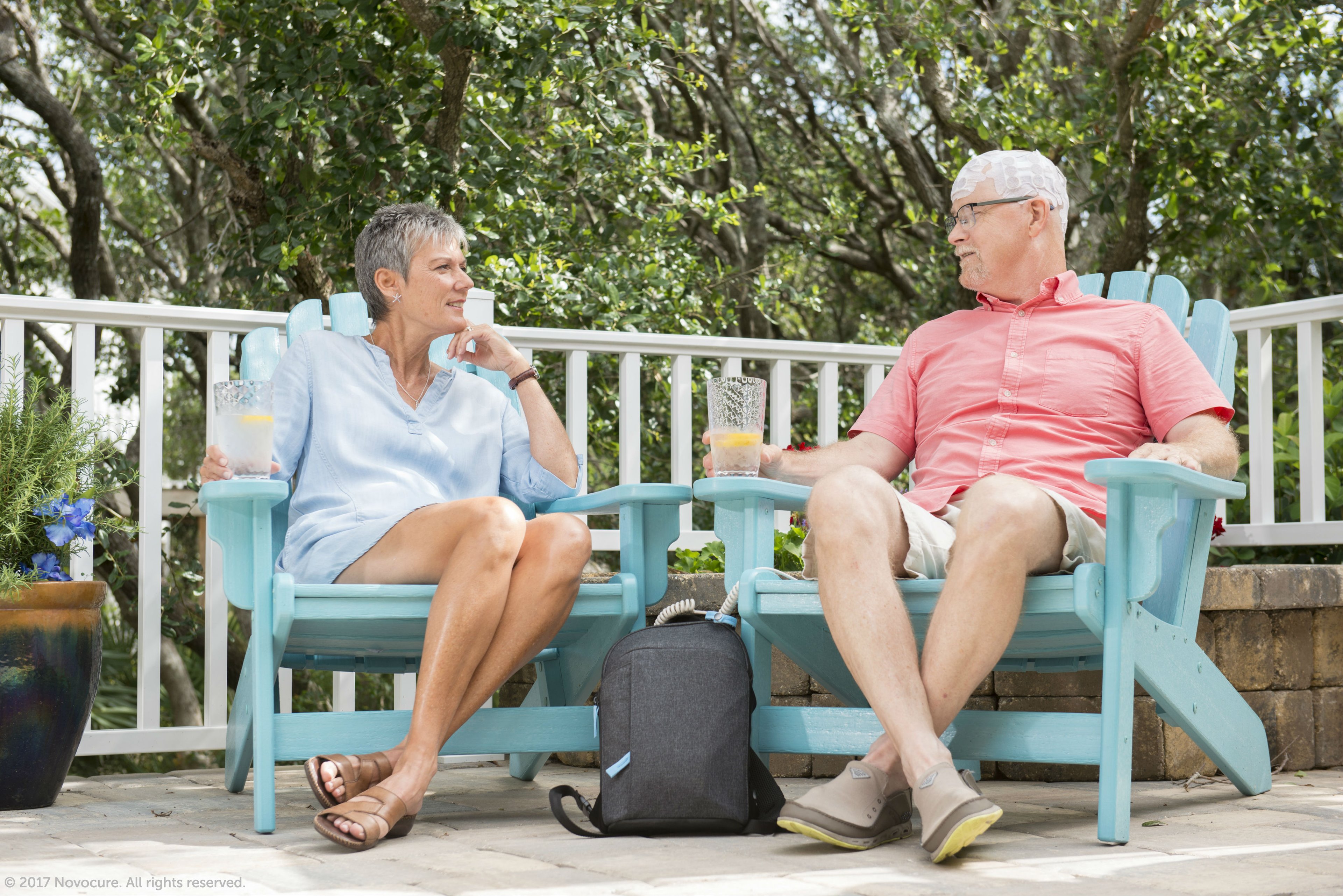 A couple sitting together on a deck with the man using an Optune device.