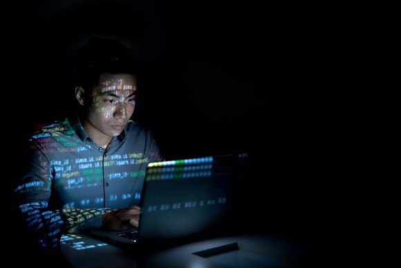 A man sitting in front of a computer in a dark room with the screen reflecting off him.