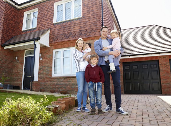 A young family poses for a photo in front of their home.
