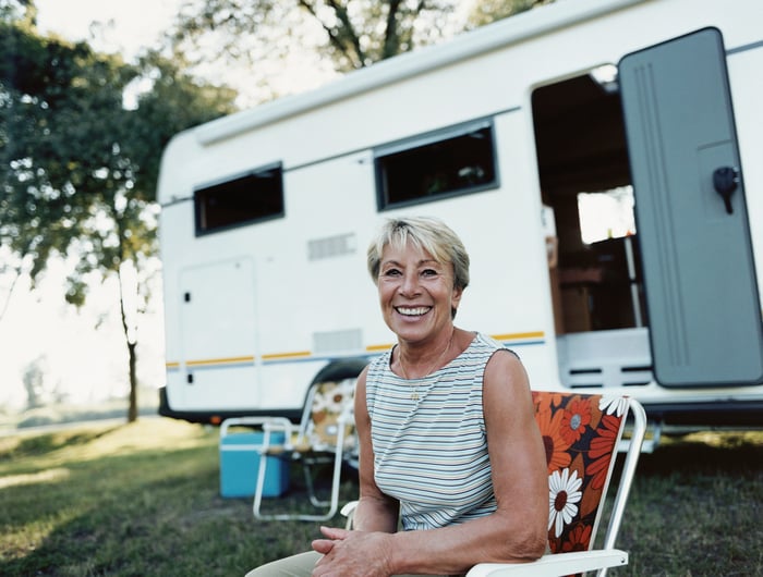 A senior woman smiling while sitting in front of a camper