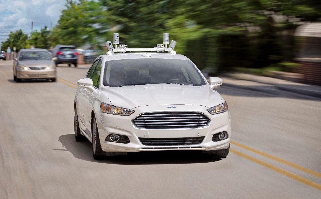A Ford sedan driving on the road with sensors on top of the car.