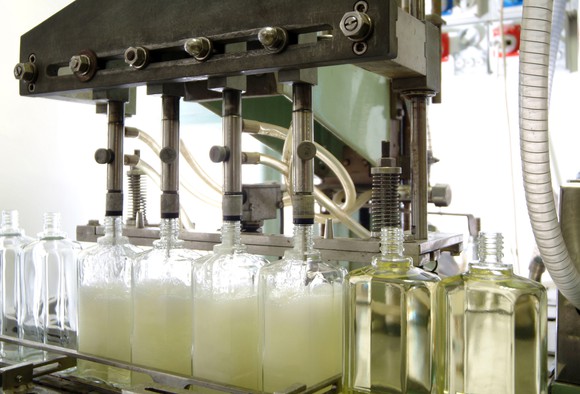 A machine at a cosmetics factory filling empty plastic bottles with liquid.