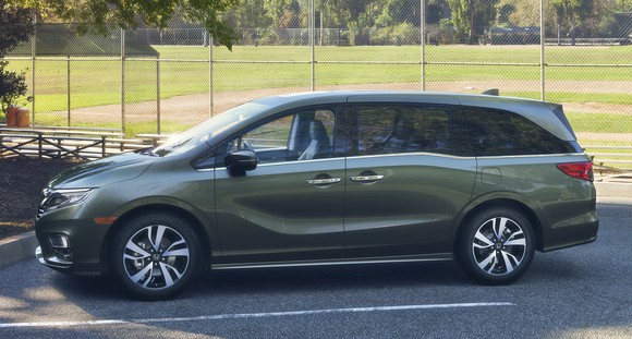 A green 2018 Honda Odyssey minivan is parked next to a baseball field. 