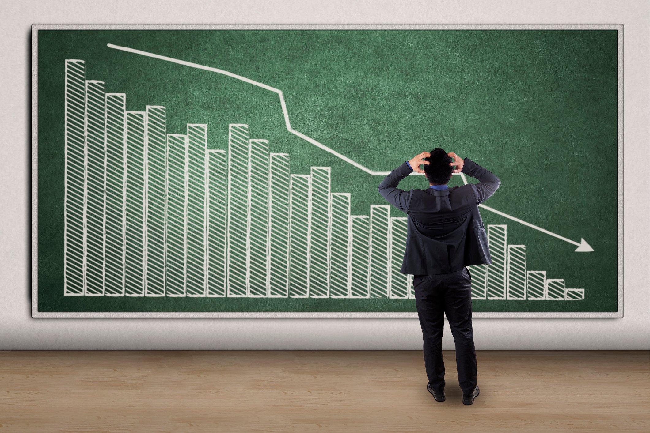Frustrated man in front of a chalkboard drawing of a downward-sloping chart.