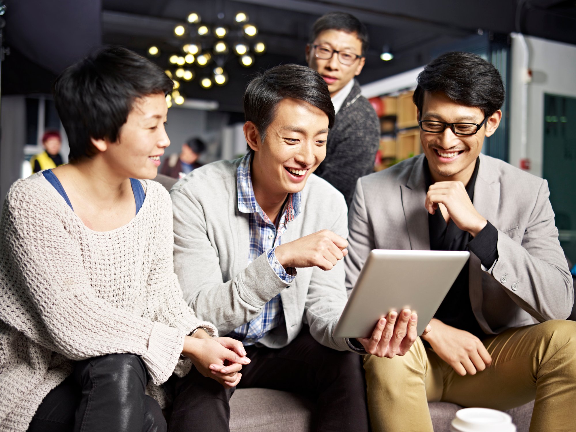 Four Asian people smiling while looking at a tablet.