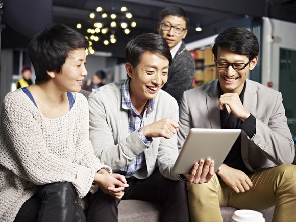 Four Asian people smiling while looking at a tablet.