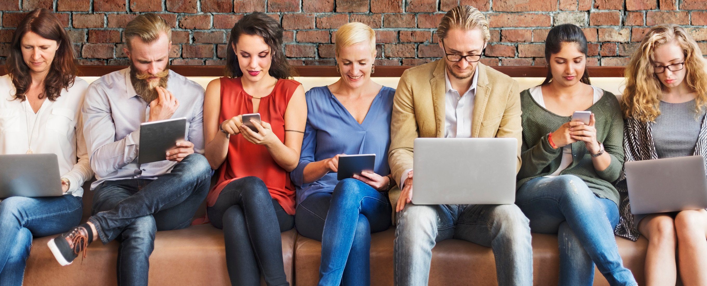 Men and women packed into a long couch, looking at laptops, tablets, and smartphones.