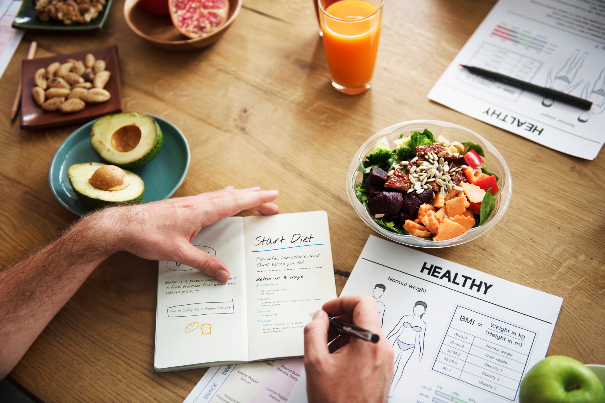 A man making notes in a notebook with dishes of healthy foods around the table.