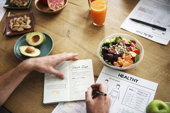 A man making notes in a notebook with dishes of healthy foods around the table.