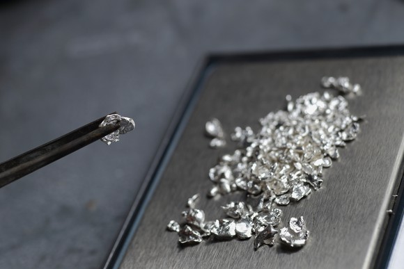 Shavings of platinum rest on a metal sheet in the background, while forceps hold a sizable piece in the forefront.