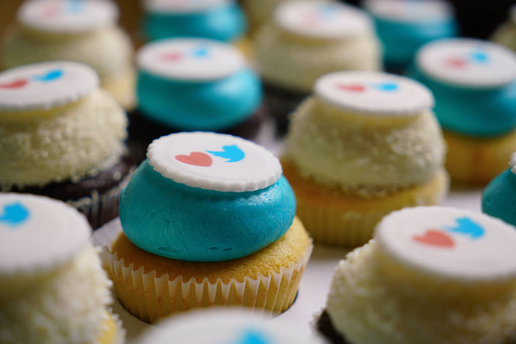 Cupcakes, half with blue frosting, half with white frosting, each under a cookie with a heart and Twitter logo on top.