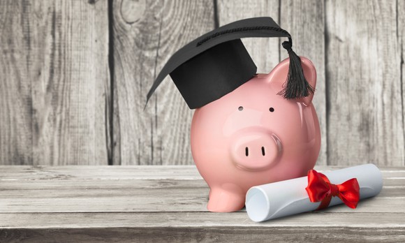 Piggy Bank wearing a graduation cap next to a rolled-up diploma