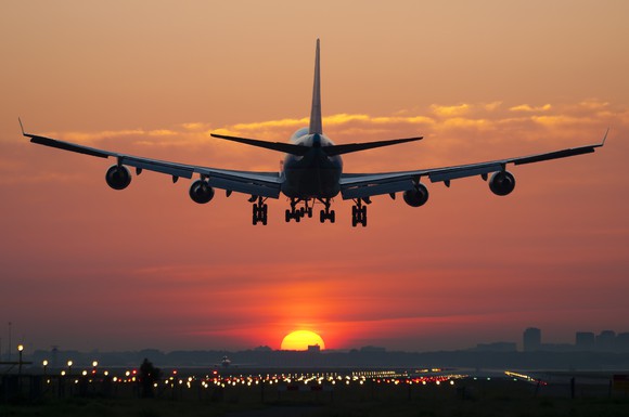 A commercial jet lands on a runway with the setting sun in the background.