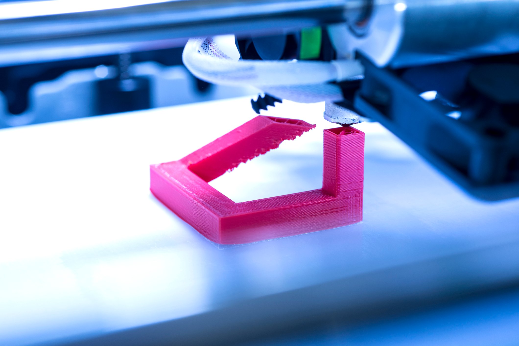 Close-up of a 3D printer printing a fuschia-colored plastic object. 