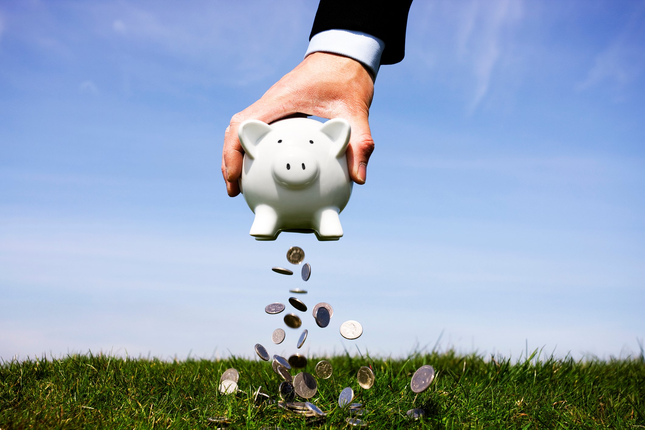 Hand shaking money out of a piggy bank.