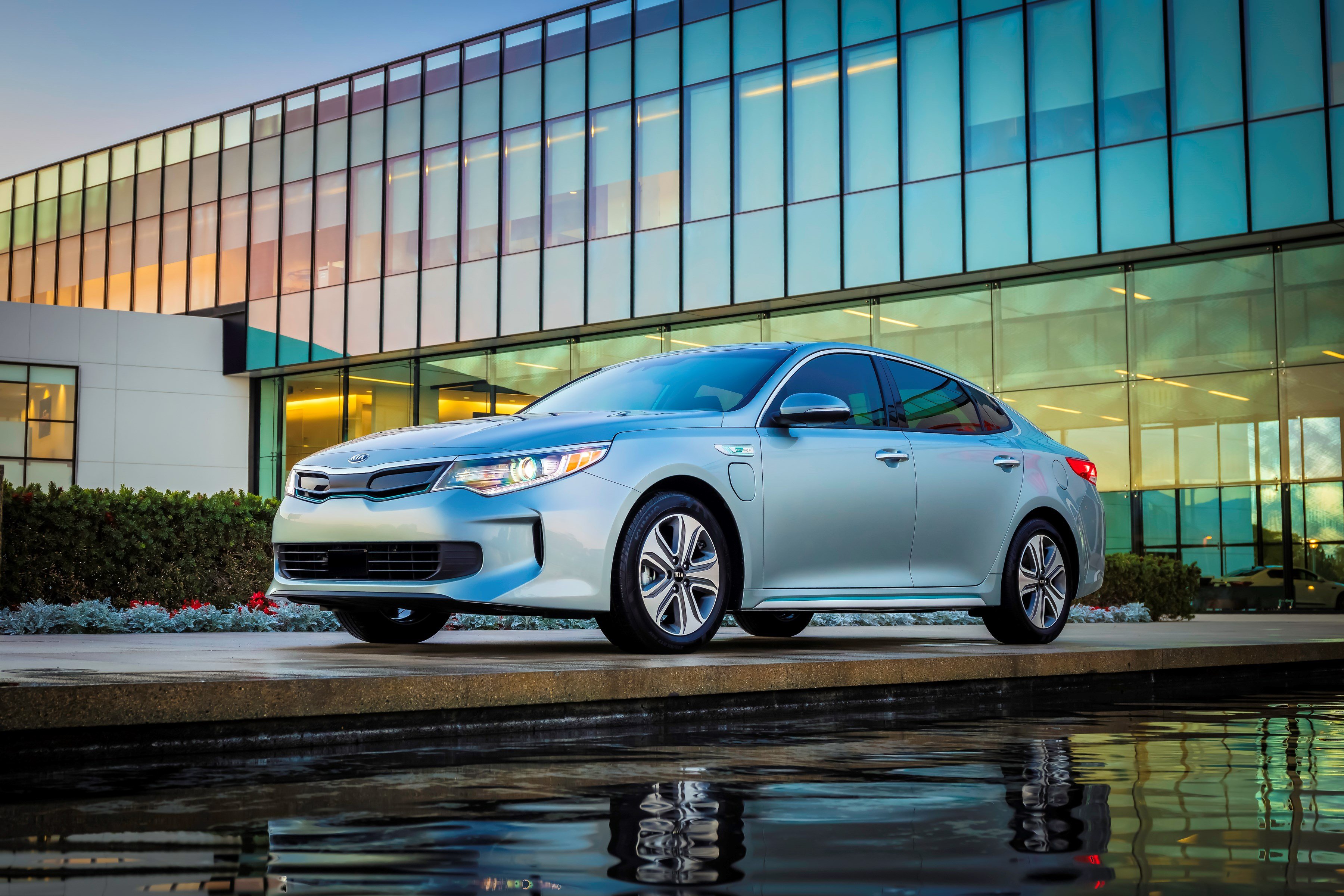 A 2017 Kia Optima Plug-in Hybrid sedan in silver, in front of a glass-paneled office building.