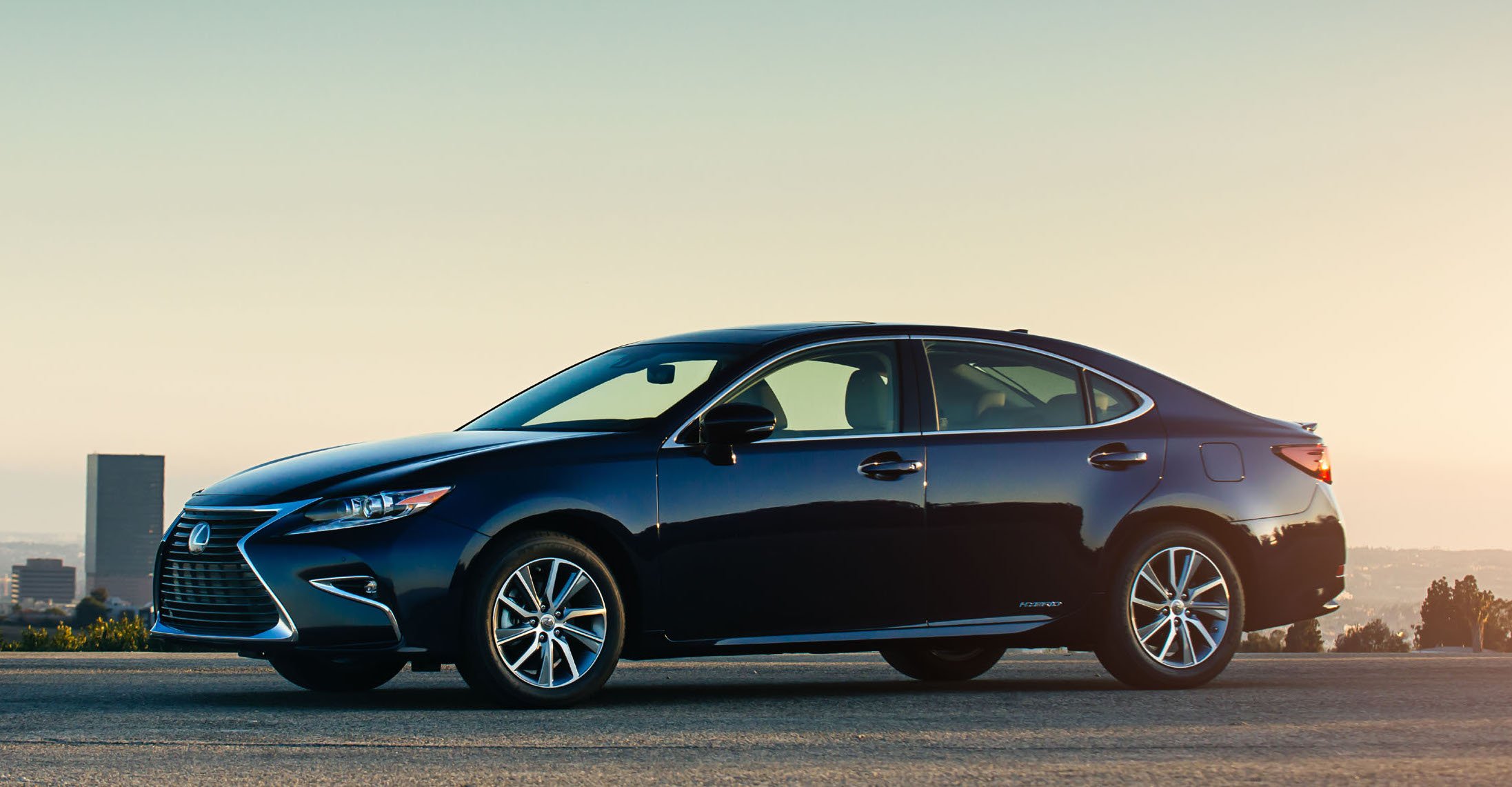 A black 2017 Lexus ES 330h sedan, in early morning light with a city in the background. 