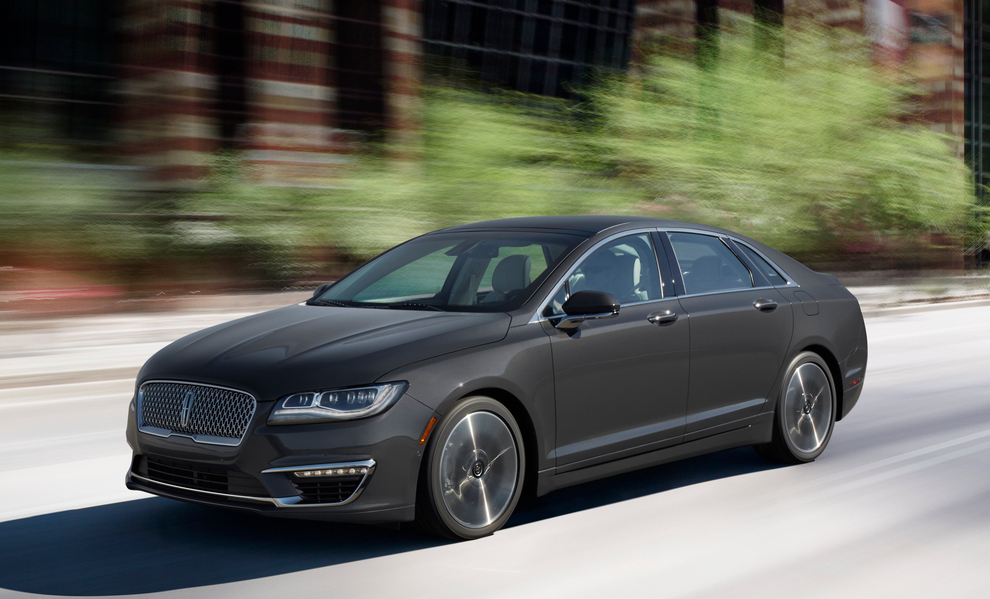 A 2017 Lincoln MKZ in dark gray on a wooded road.  