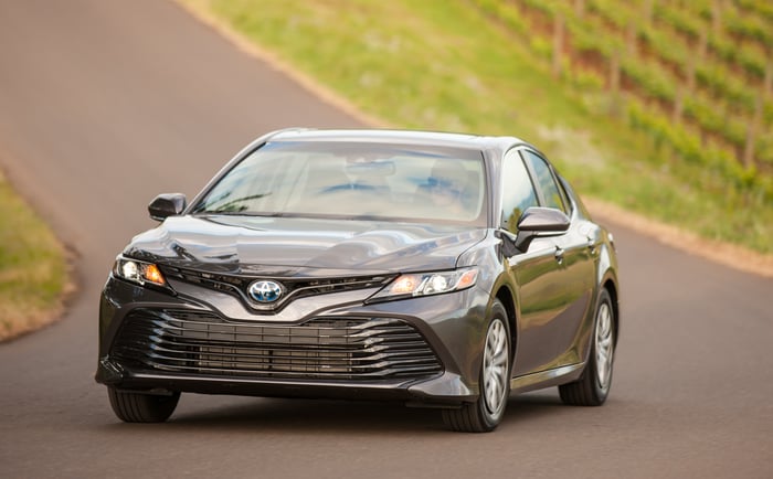 A 2018 Toyota Camry Hybrid in dark bronze, on a country road.