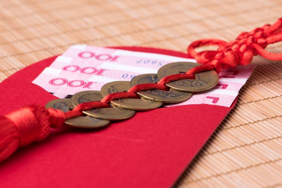 Chinese lucky coins on top of Chinese banknotes inside an open red envelope.