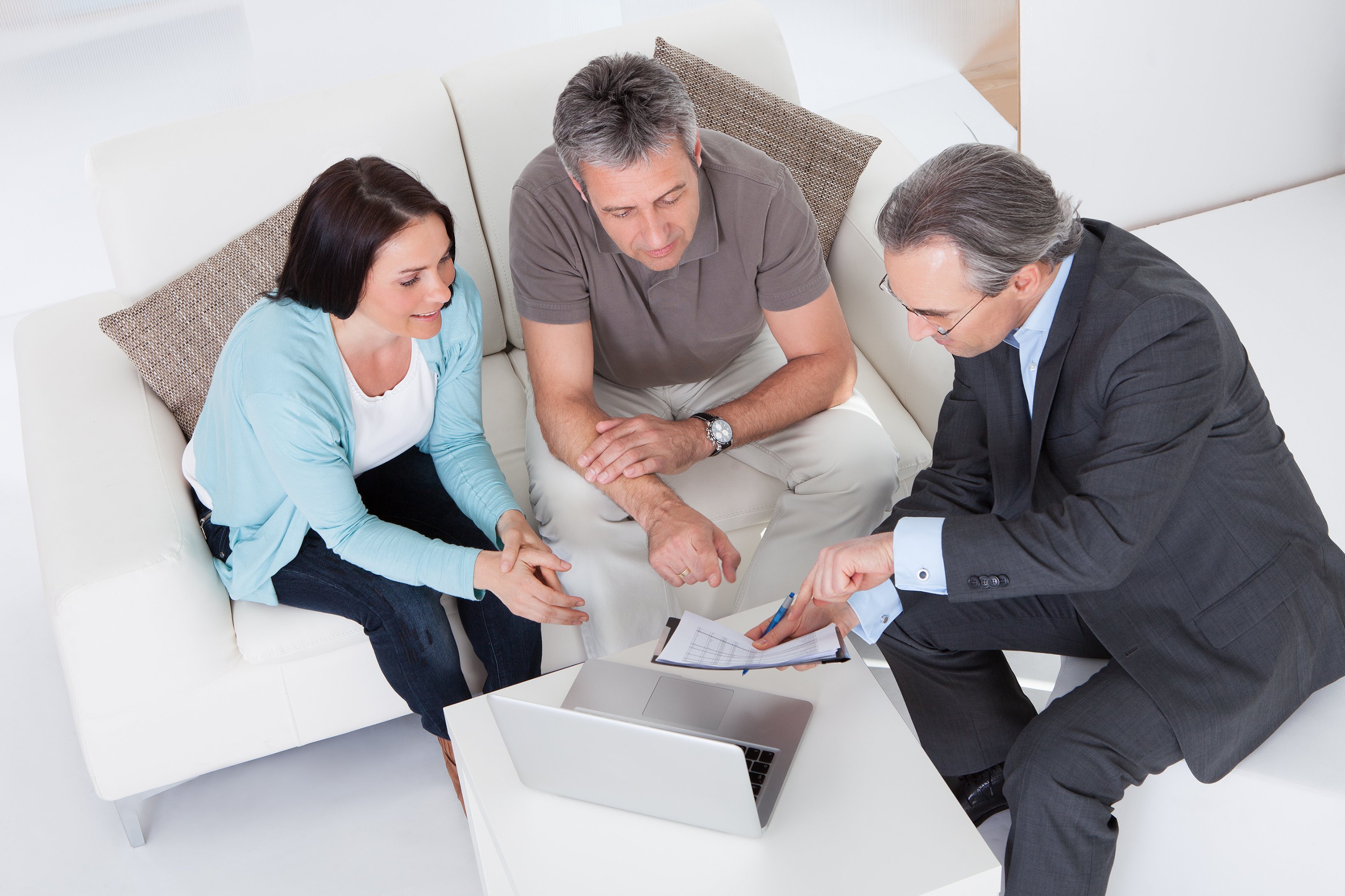 Meeting between person in suit and two people in more casual clothes, around a table with papers and a laptop.