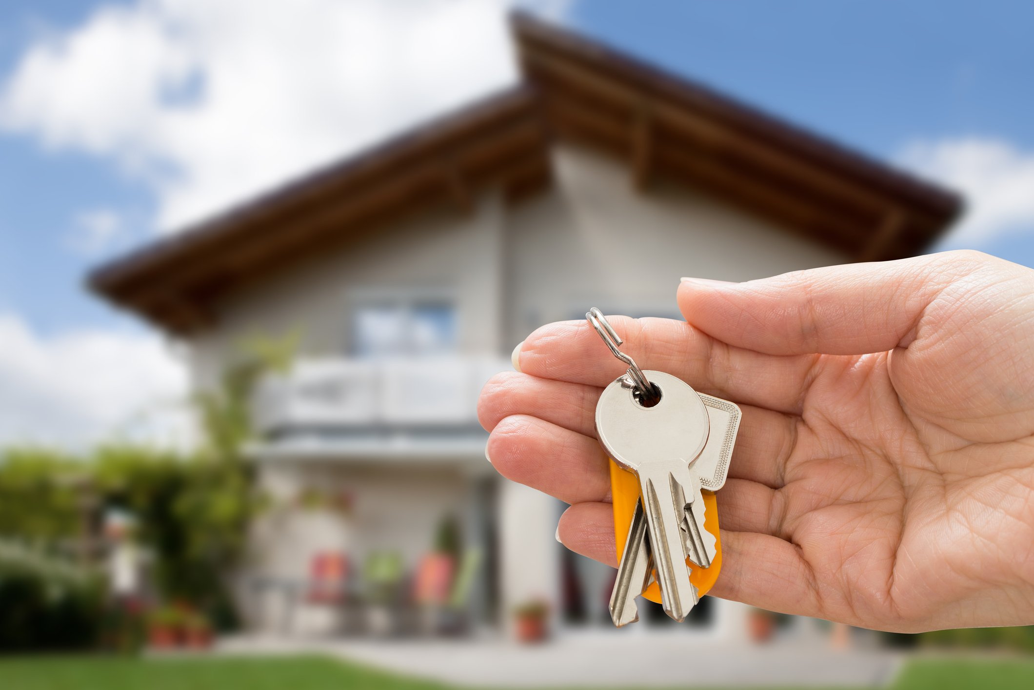 Hand holding house keys with a home in the background