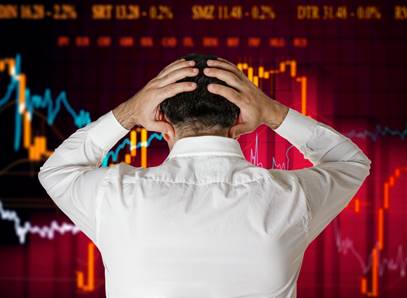 A man holds his head in his hands as he stares at a screen showing a declining stock price.