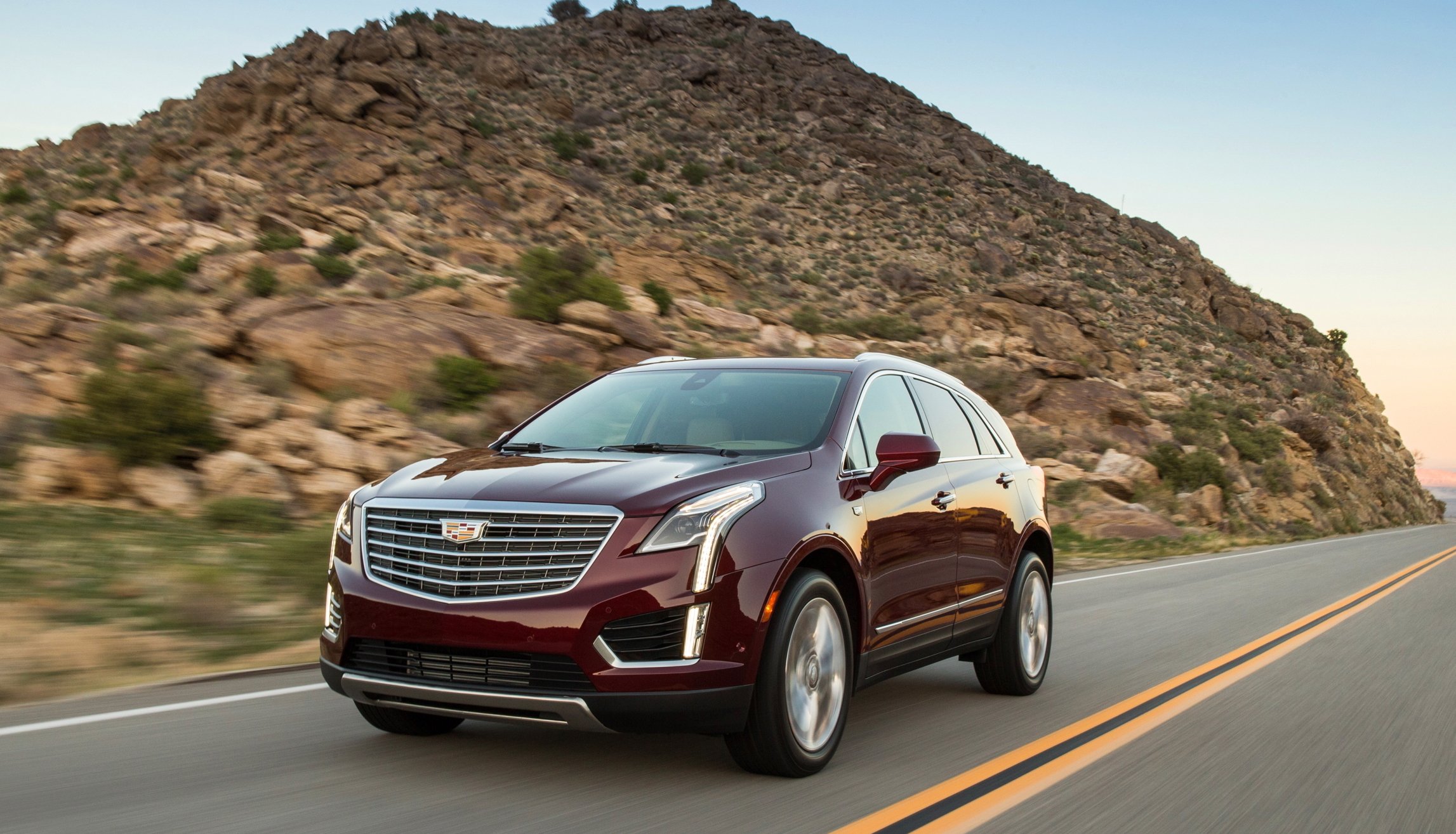 A dark red Cadillac XT5 on a road near a rocky hill.
