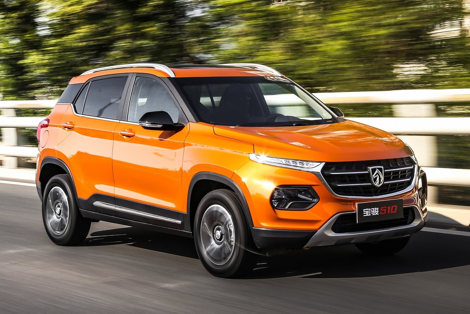 An orange Baojun 510 compact SUV, at speed on a country road. 