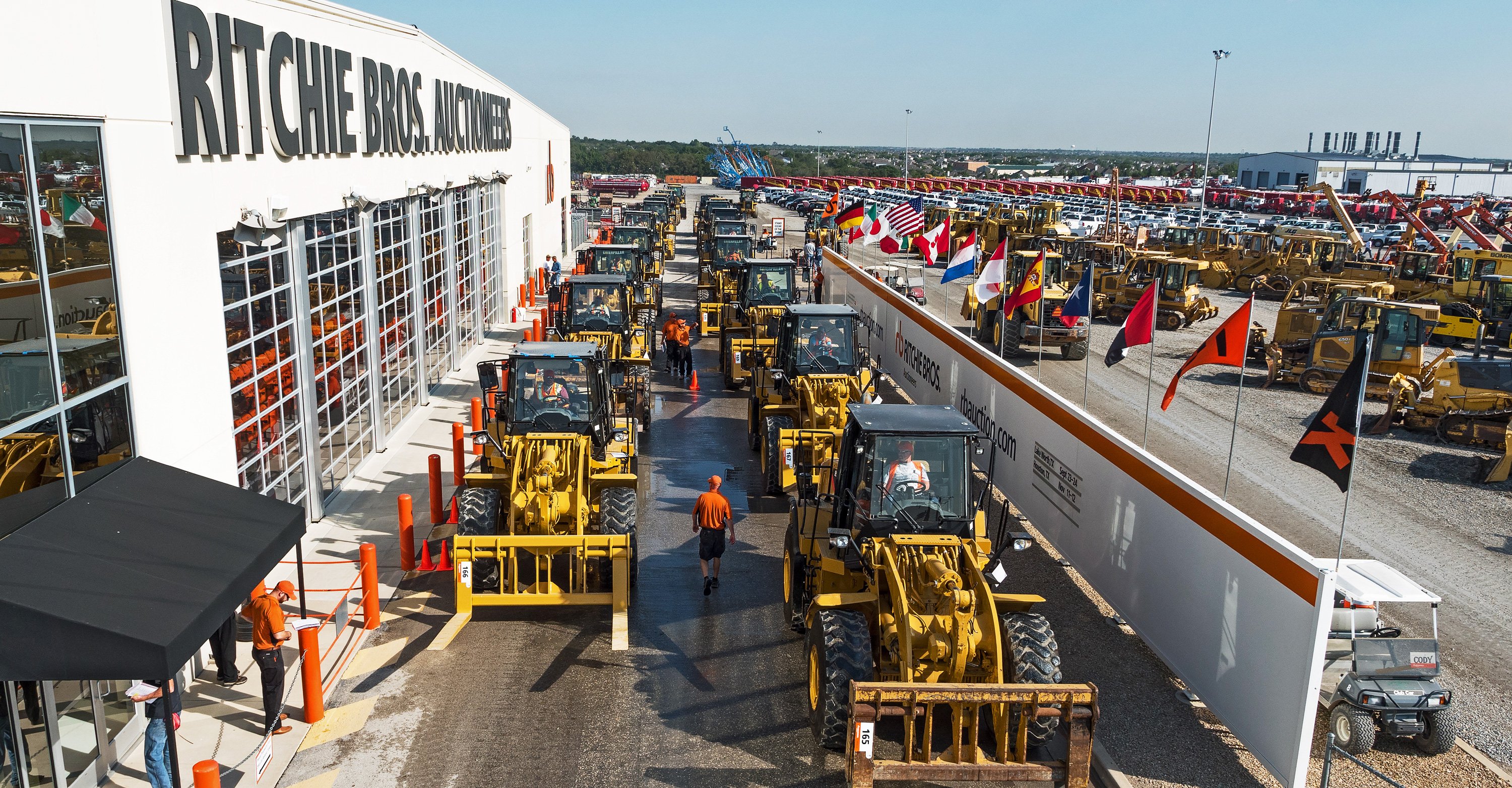 Heavy equipment lined up in front of building with Ritchie Bros. sign.