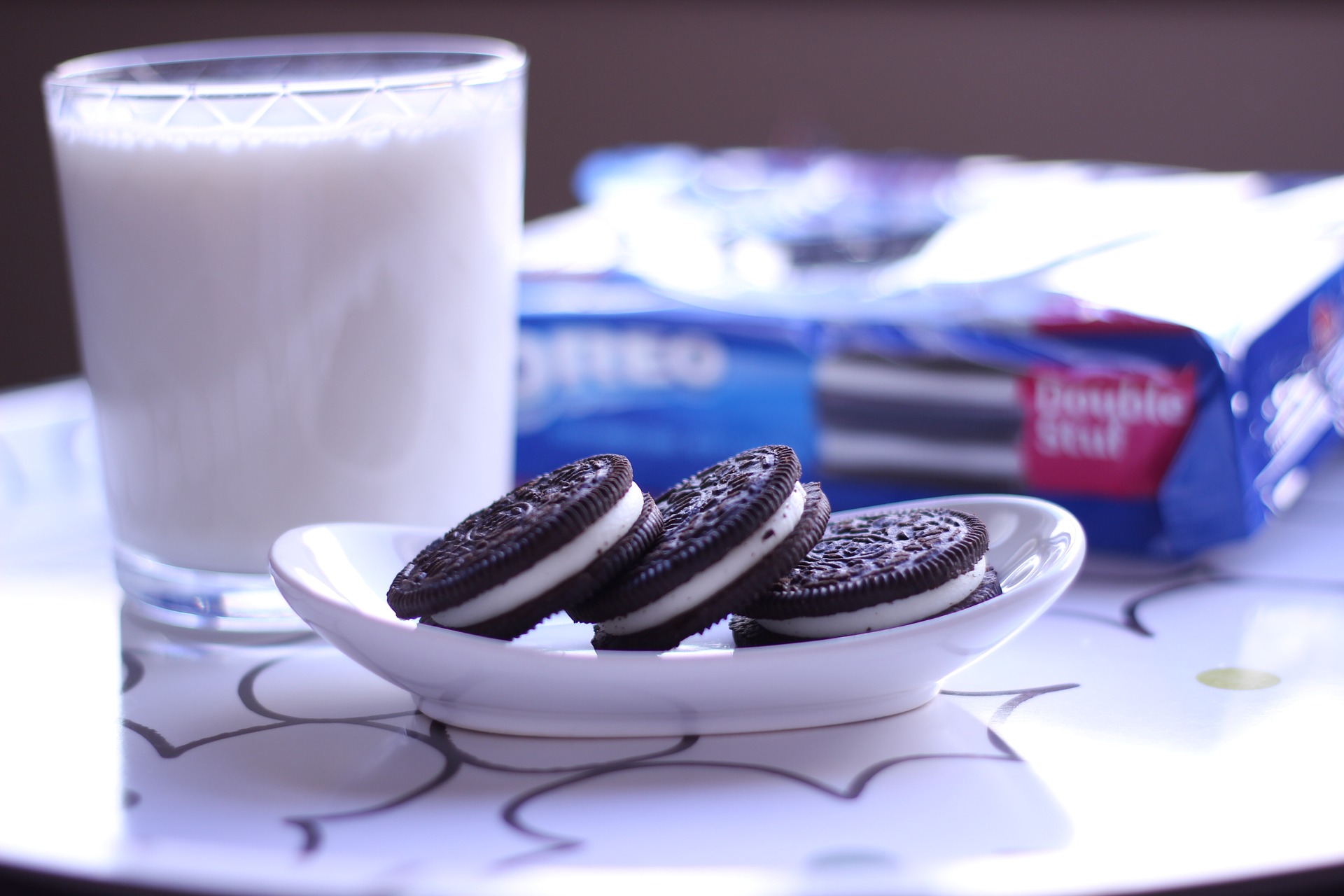 A plate of Oreo cookies and a glass of milk with an Oreo branded package in the background.