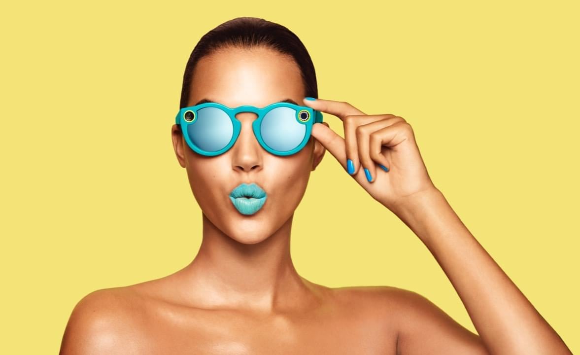 A woman wearing turquoise Snap Spectacles and matching lipstick.