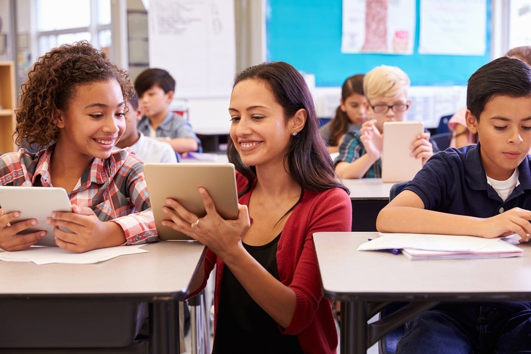 Teacher in a classroom showing a tablet to a student.