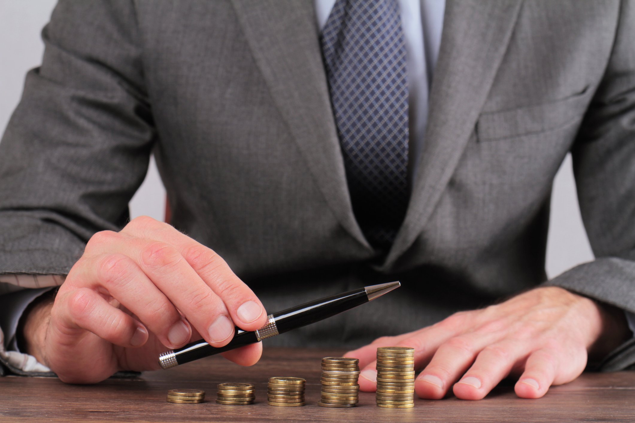 Progressively larger stacks of coins with a man pointing in a similarly upward direction with a pen.