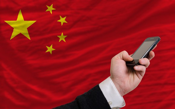Hand holding mobile device in front of China's national flag.